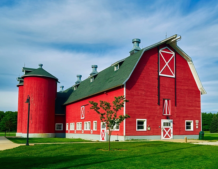 A red barn with two silos in the middle of it.