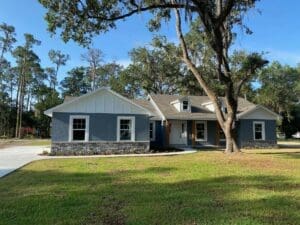 A blue house sitting under a tree in the grass.